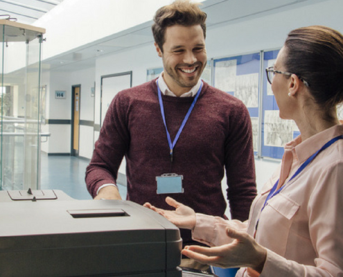 Two workers smiling and talking by the copier
