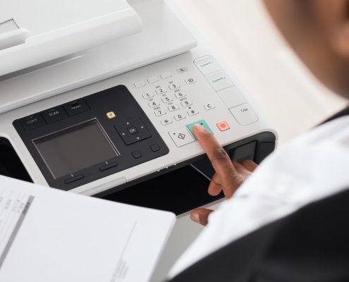 View over woman's shoulder while she presses start button on office copier
