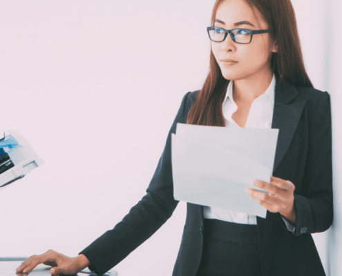 Woman holding pieces of paper as she looks at the office copier