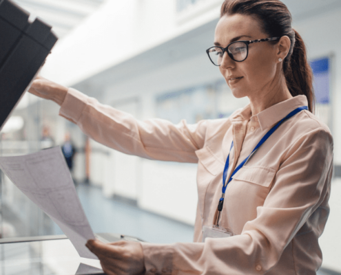 A woman in a blue lanyard looking at documents in front of a printer