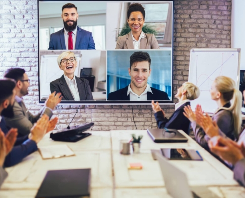 A boardroom meeting with four employees projected on a screen