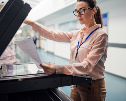 Side view of school faculty member copying sheet on printer