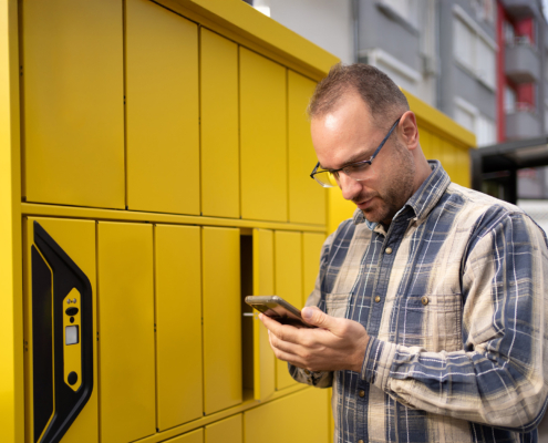 Man using smartphone near bright yellow parcel lockers in urban setting